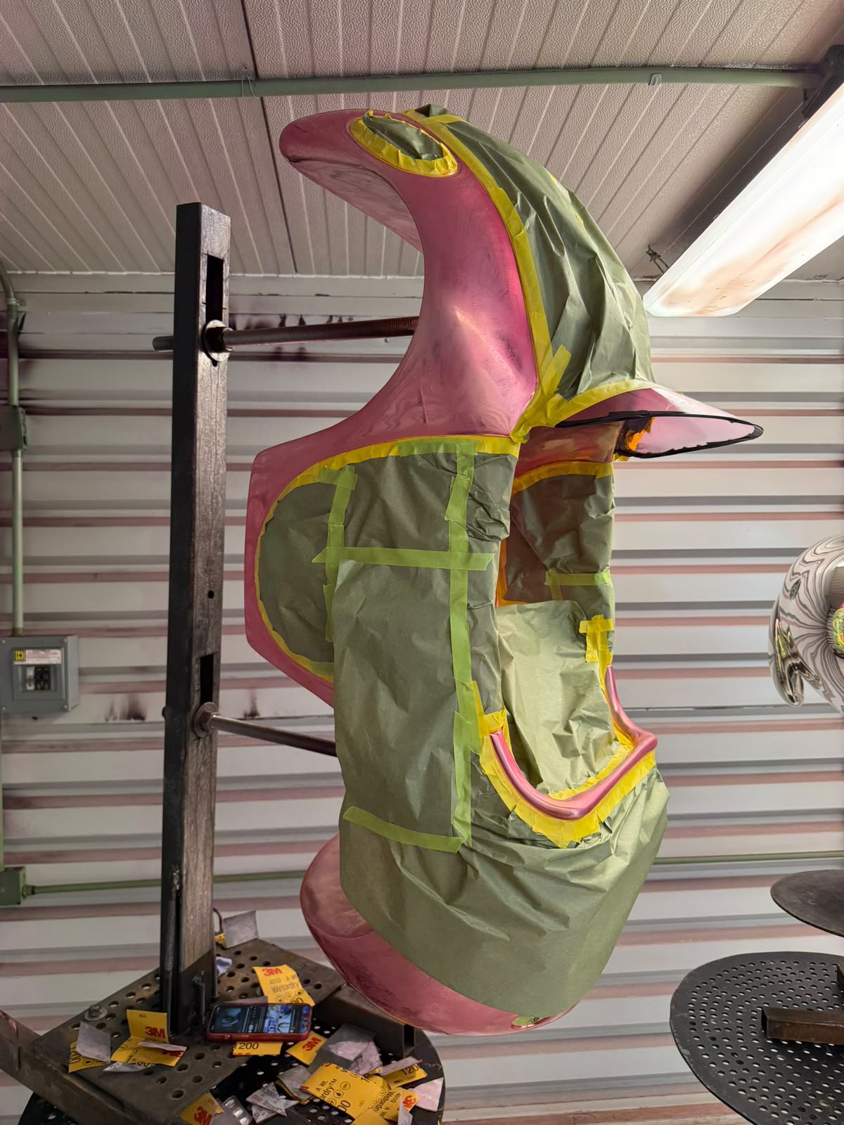 Escultura de Hermes rosa parcialmente cubierta con papel y cinta durante el proceso de color